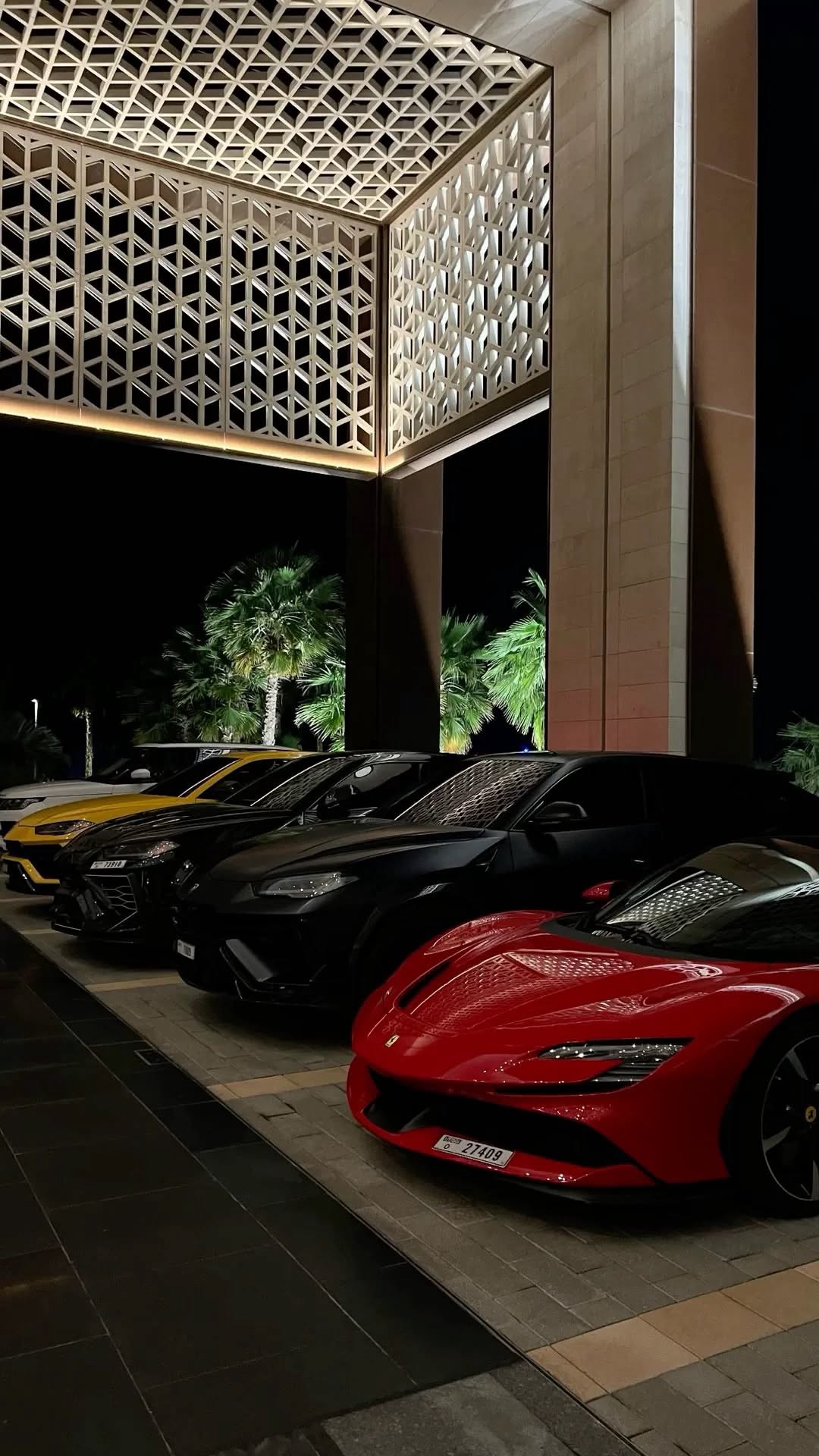 Row of supercars parked outside a lit hotel entrance