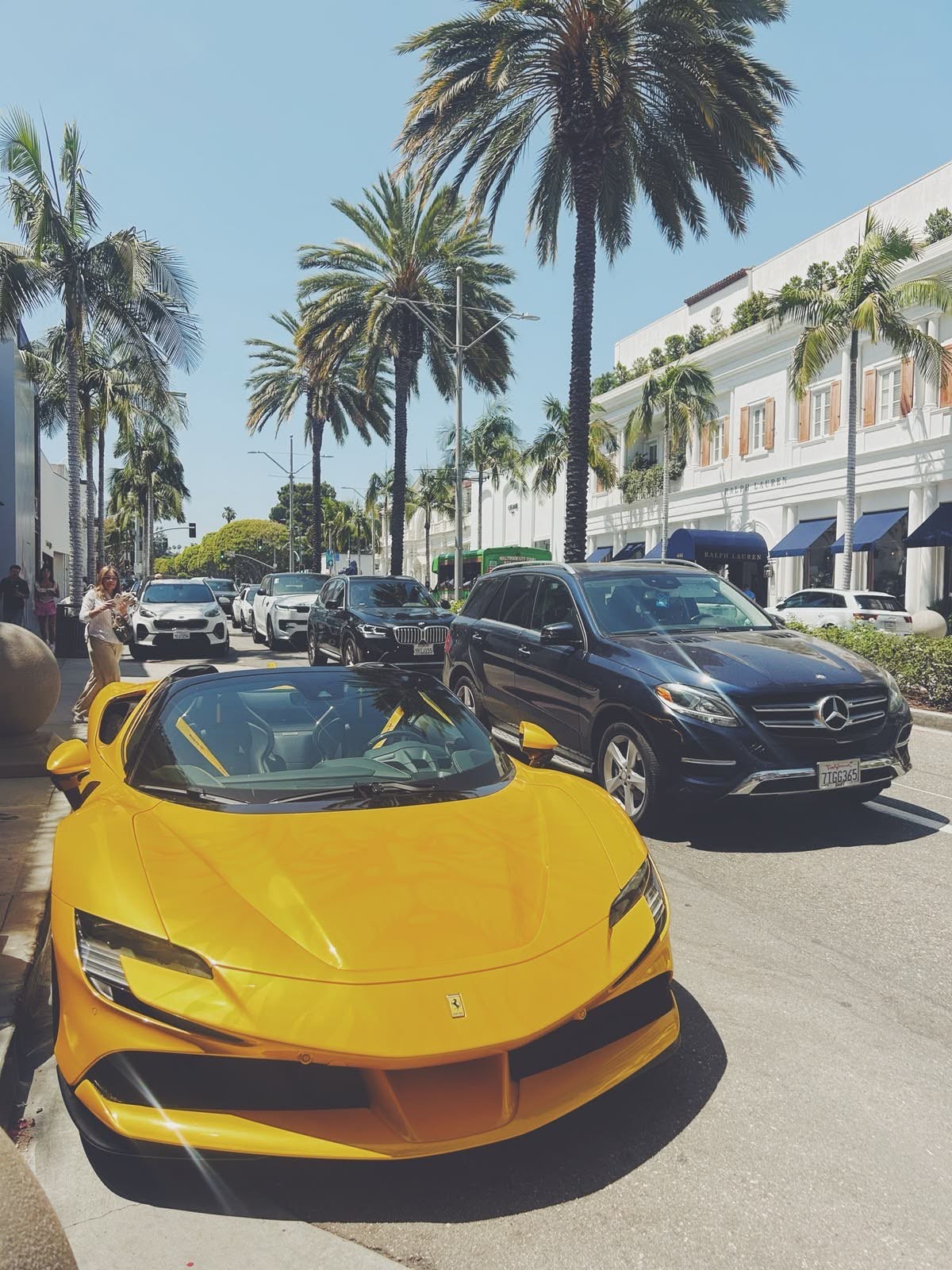 Yellow supercar on a palm-lined shopping street in daylight